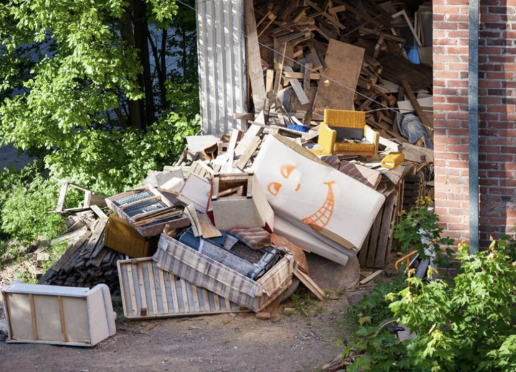 A disorganized pile of furniture and various items stacked outside a building, indicating a potential move or cleanup.