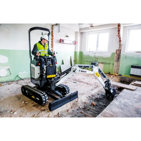 Compact mini excavator performing interior demolition inside a commercial building, removing flooring and debris in a confined space.