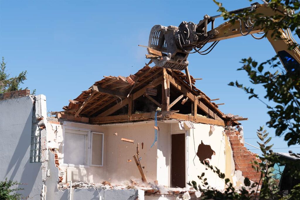 Excavator demolishing a small residential structure during controlled demolition project