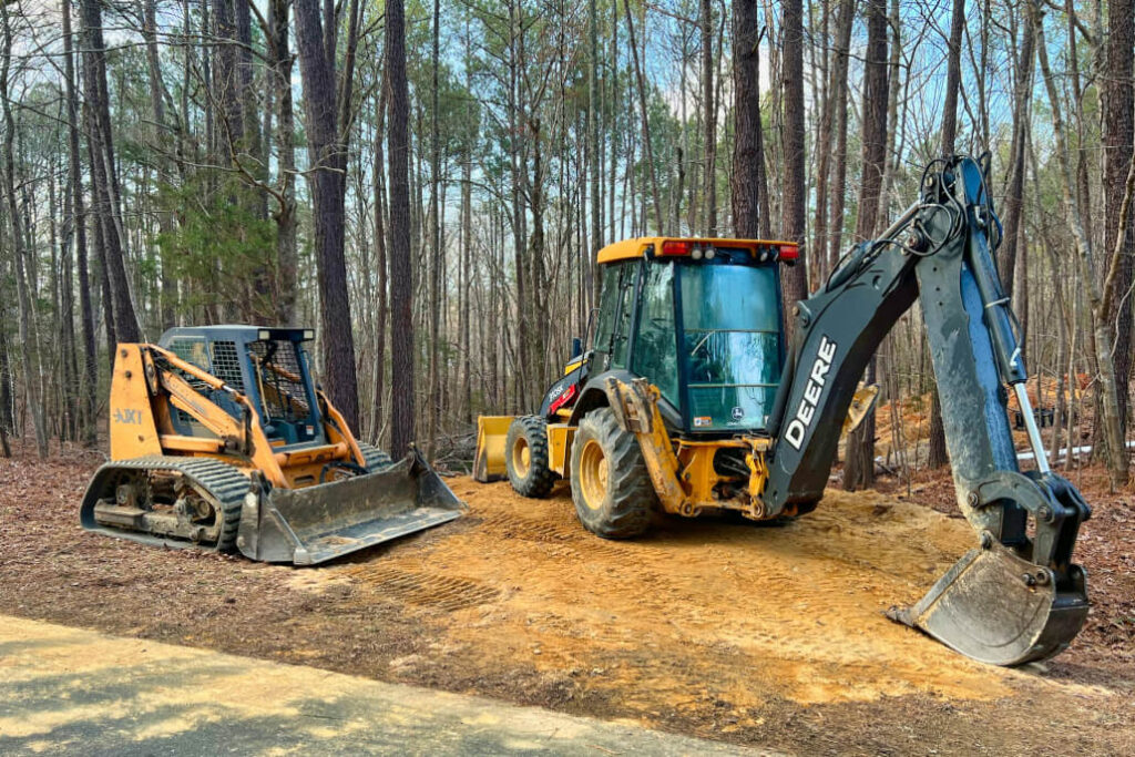 A backhoe and a front loader parked among trees in a wooded area, showcasing heavy machinery in a natural setting.