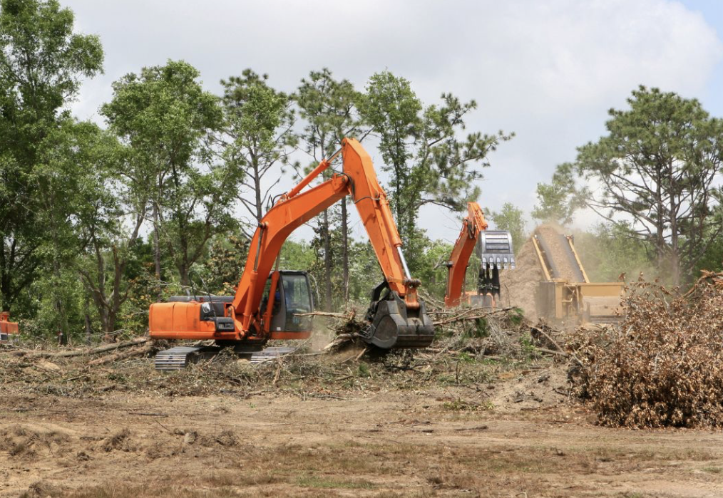 A large orange excavator operates on a dirt pile, showcasing heavy machinery in construction work.