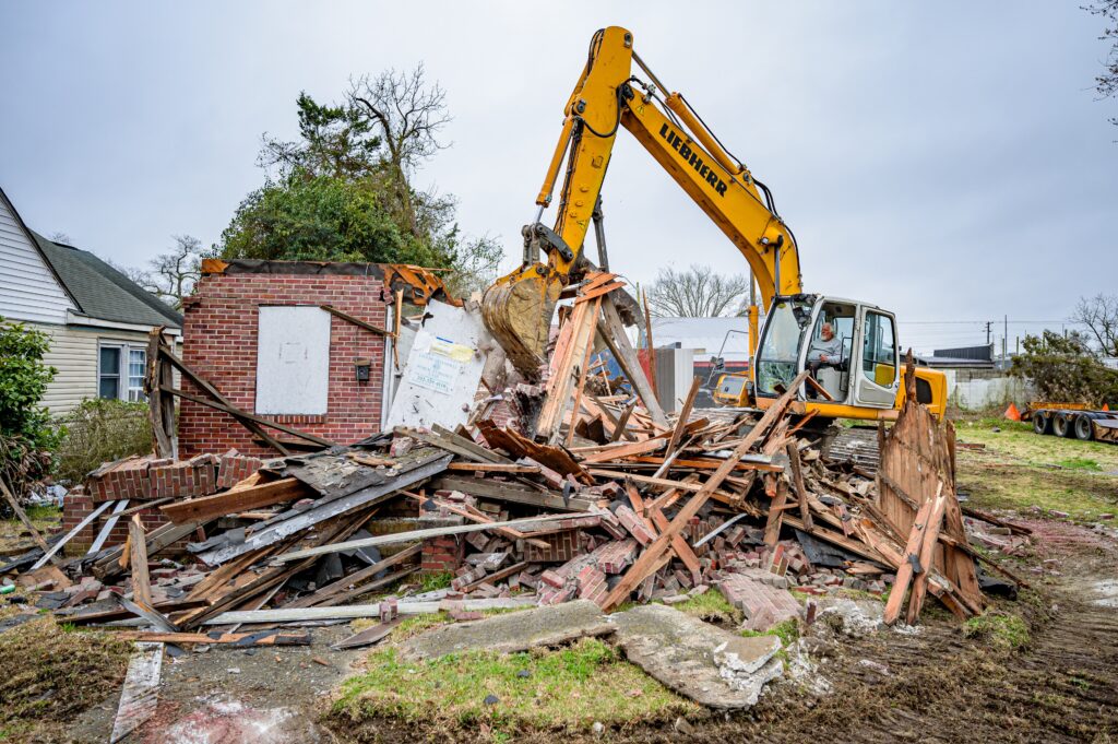 Heavy machinery demolishing a vacant house with demolition debris in foreground