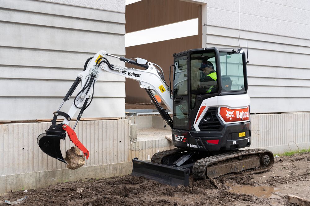 Bobcat compact excavator equipped with a hydraulic demolition attachment working beside an industrial building for precision demolition.