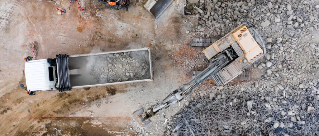 Concrete removal and site clearing process with excavator bucket and debris